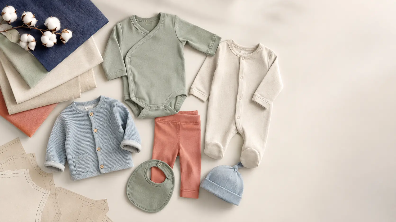 Coordinated newborn and toddler garments laid out with soft fabric swatches